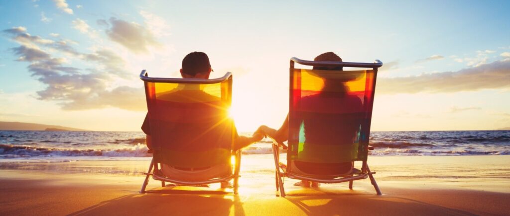 A happy couple sitting on the beach at sunset.