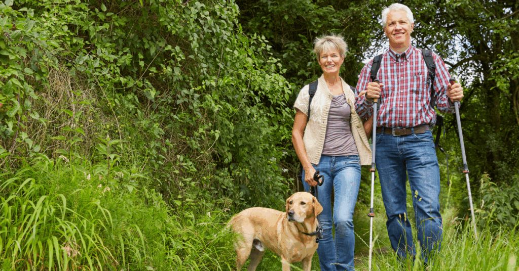 A retired couple hiking with their dog on a wooded trail, representing purpose-first planning for families and a calm, confident retirement.