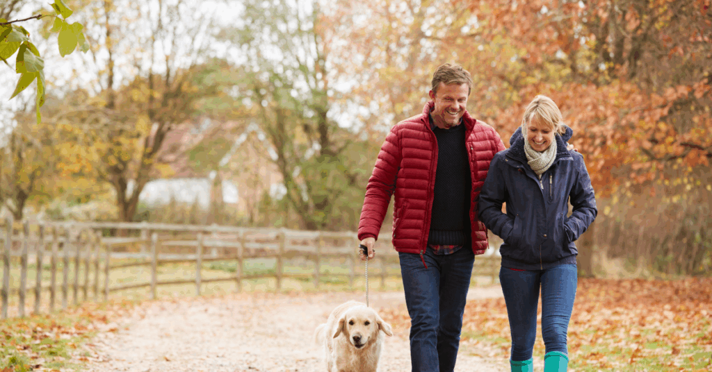 Couple walking together with their dog on a tree-lined path in autumn