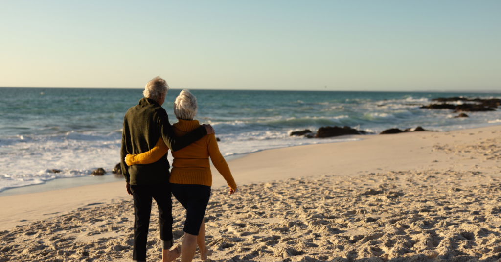 Older couple walking along the beach at sunset, reflecting on what matters most in retirement.