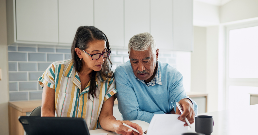 Couple in their 60s reviewing financial documents together at a kitchen table.