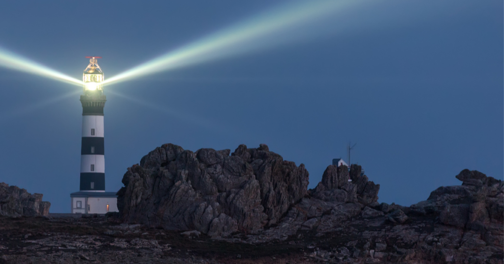 Lighthouse shining across rocky coastline at dusk, symbolizing steady guidance during market volatility