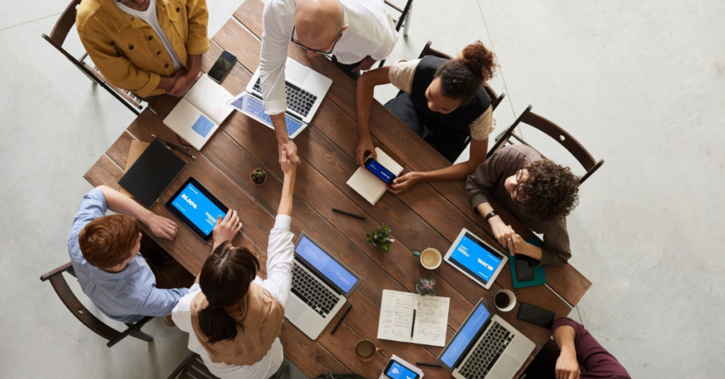 Professionals gathered around a conference table shaking hands during a team meeting